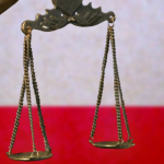 Close-up of a small bronze statuette of Lady Justice before a flag of Texas.